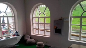 A room with large arched windows, a green mat, a white table, and a small stool. - Lizarrusti Parketxea - Hostel (Ataun)