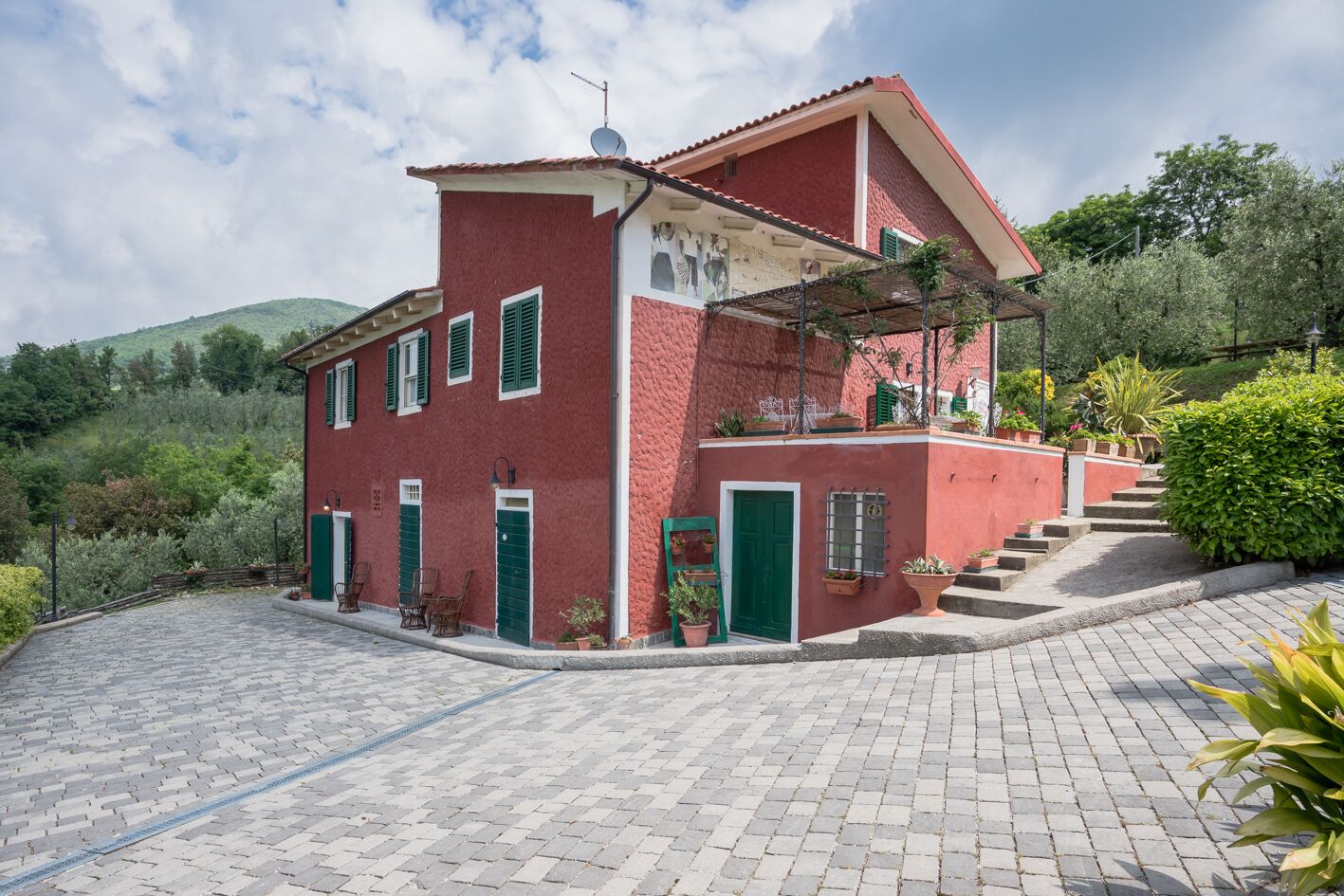 Une villa rouge avec un balcon, un escalier menant à l’entrée et une allée pavée.