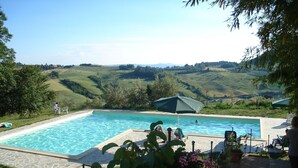 Une piscine offrant une vue sur des collines verdoyantes, entourée de végétation et dotée d’un espace extérieur aménagé pour se détendre.
