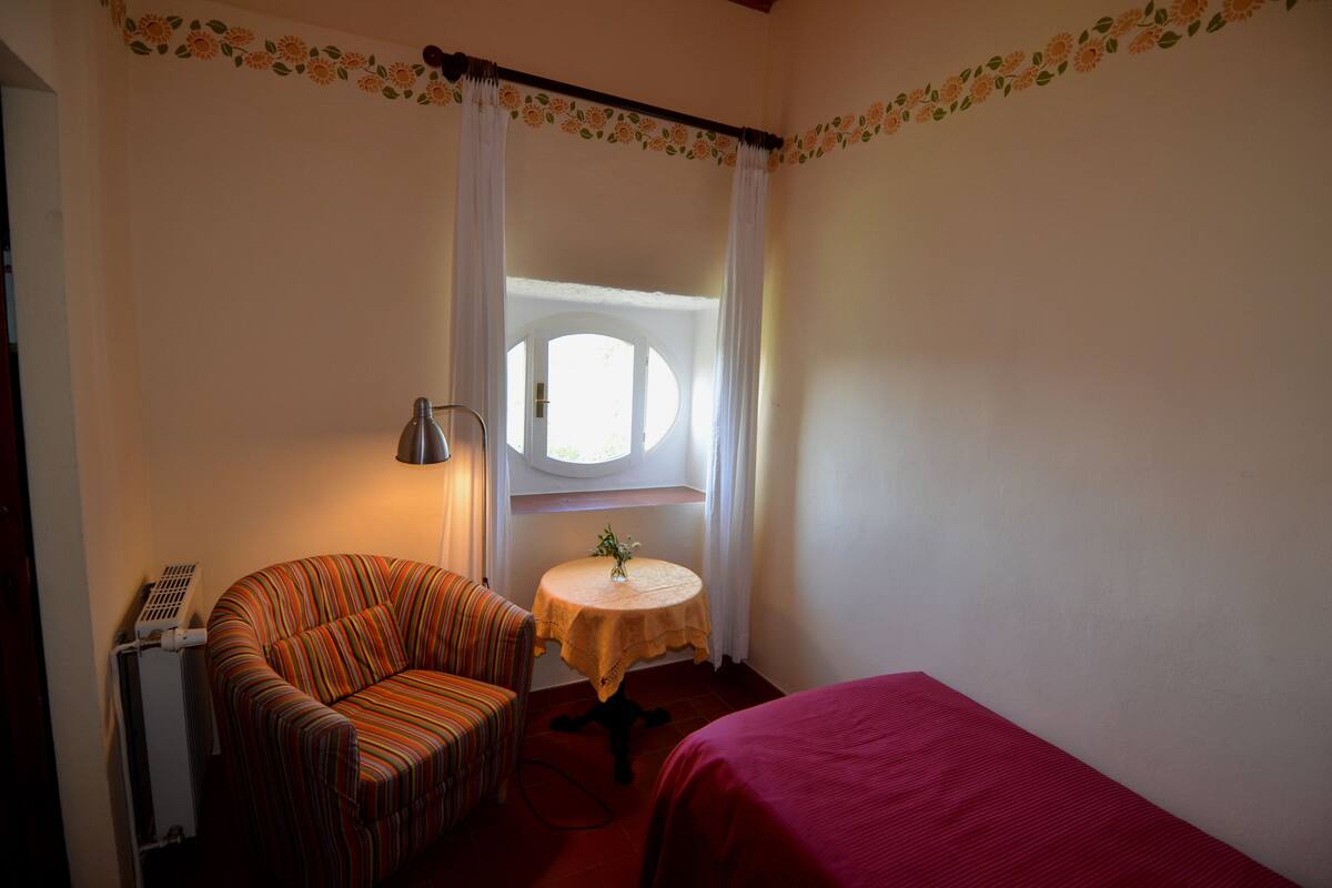 Een kamer met een eenpersoonsbed, een stoel, een tafel met een vaas en een radiator.