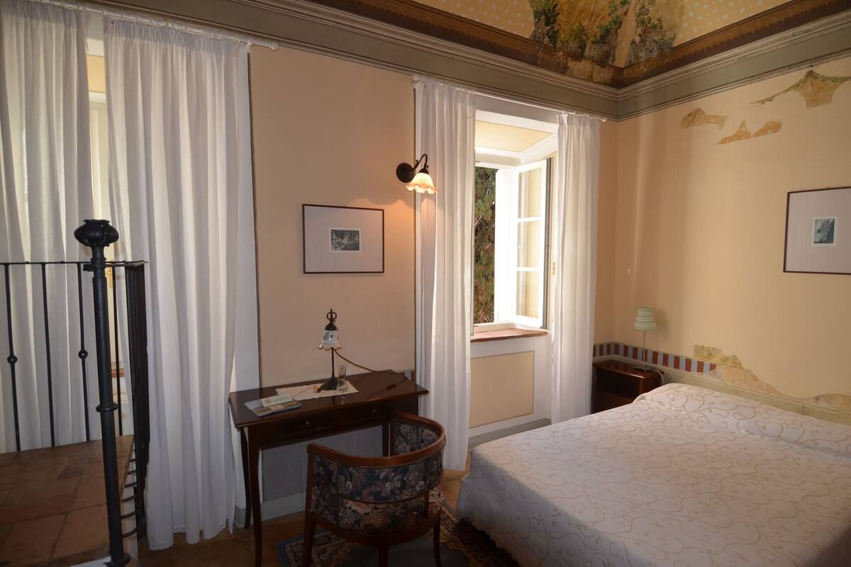Een slaapkamer met een bed, een bureau, een stoel en een raam met gordijnen.