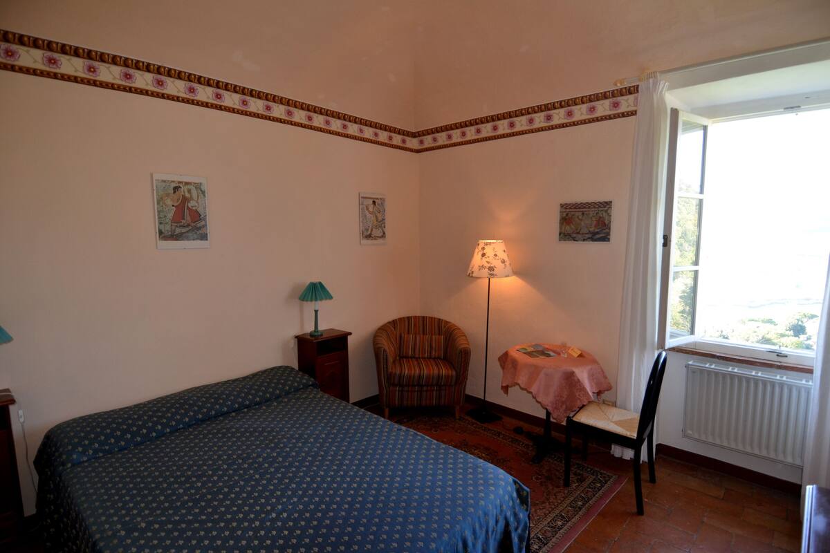 Een slaapkamer met een bed, een stoel, een tafel en een raam.