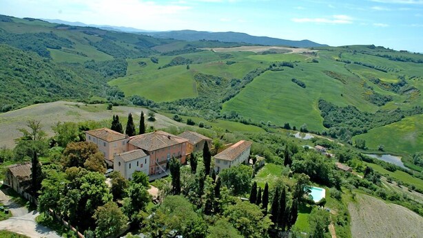 Un grand immeuble à étages, entouré d’une végétation luxuriante et de collines ondulantes.
