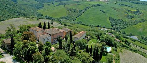 A rural villa with a courtyard, surrounded by lush greenery and rolling hills.