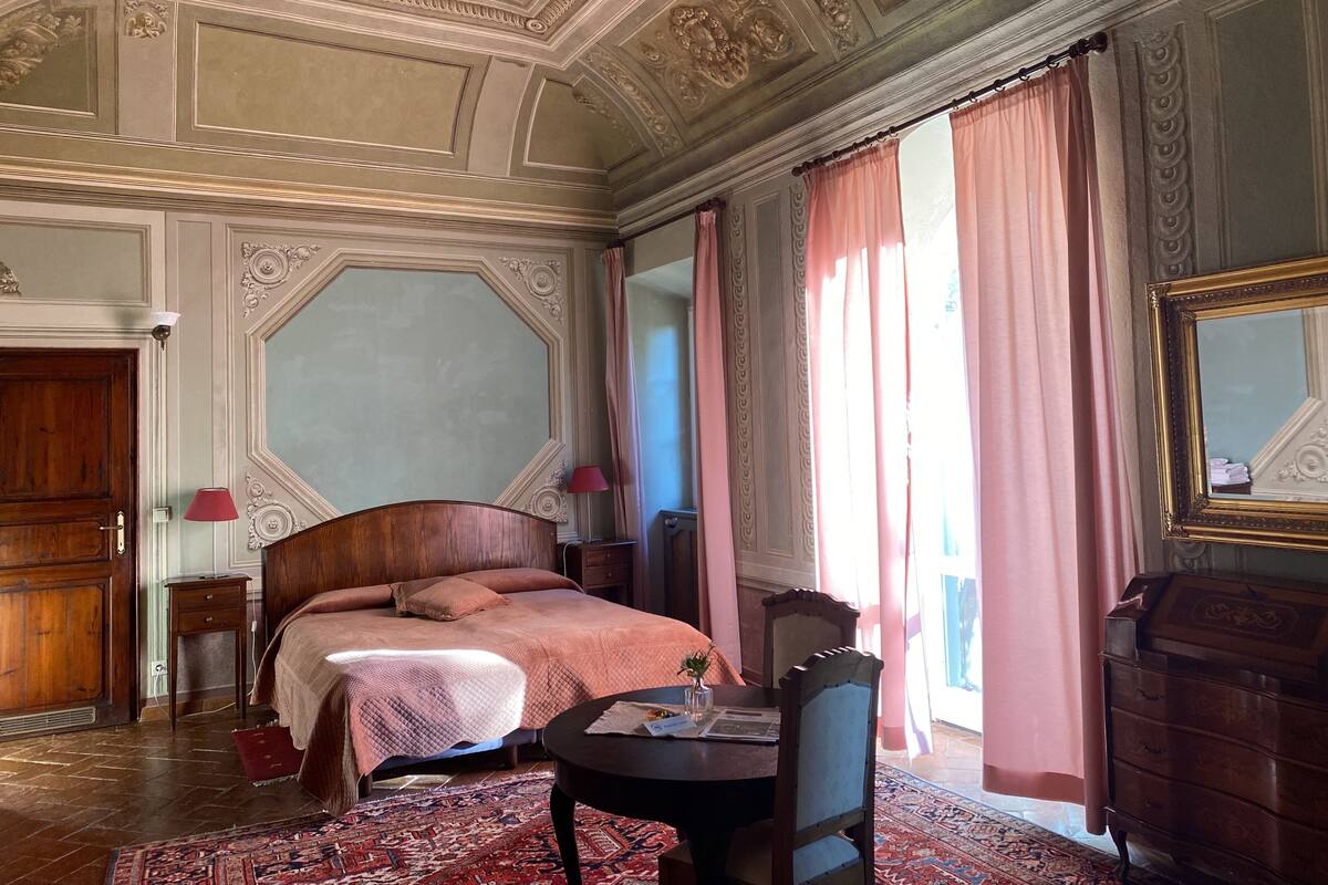 Een slaapkamer met een groot bed, een houten dressoir, een stoel en een tafel met een lamp.