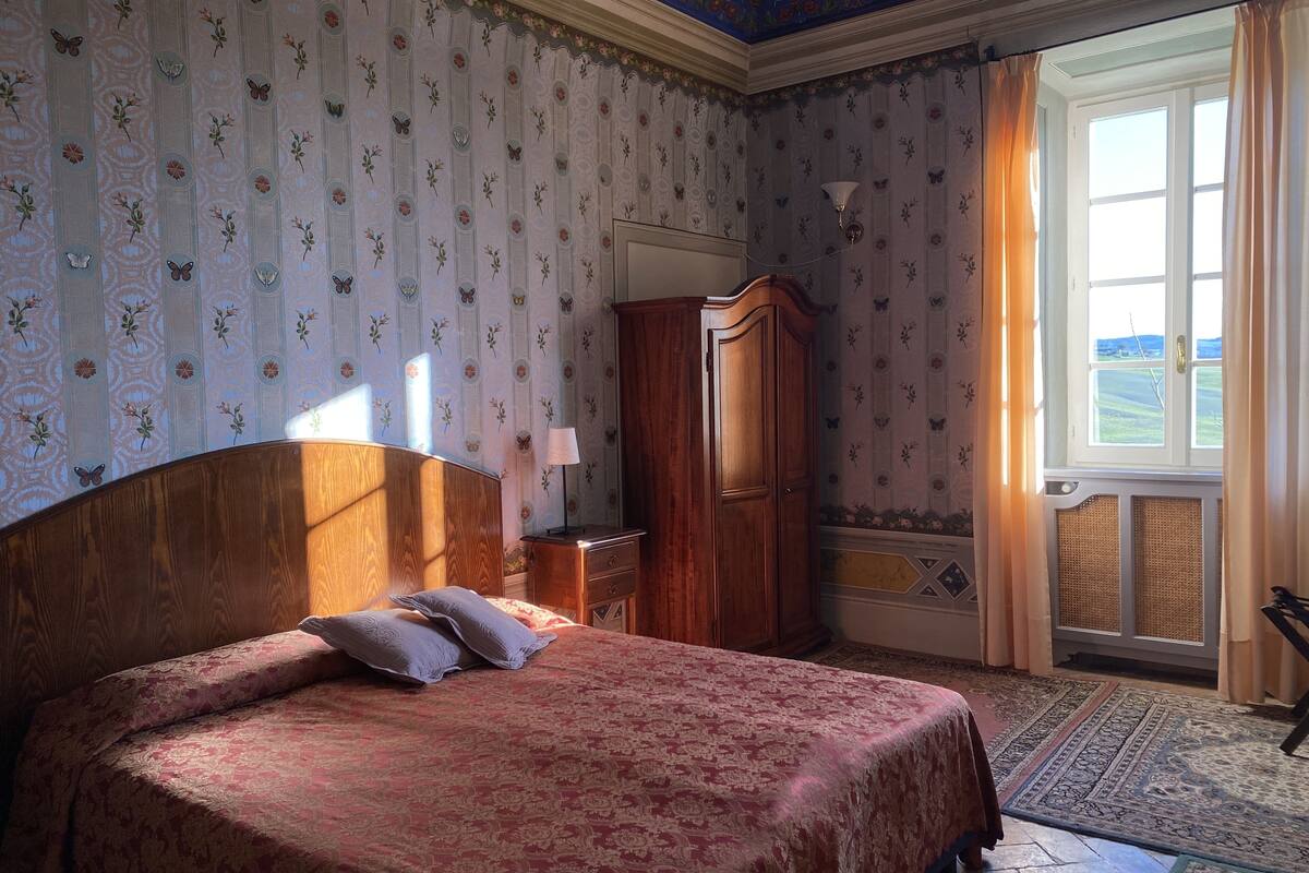 Een slaapkamer met een groot bed, een houten garderobe, een nachtkastje en een raam met gordijnen.