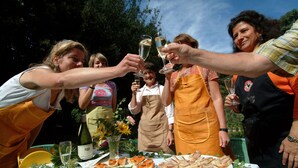 Un groupe de personnes trinquant avec des verres de vin autour d’une table en plein air, devant des assiettes remplies de nourriture.