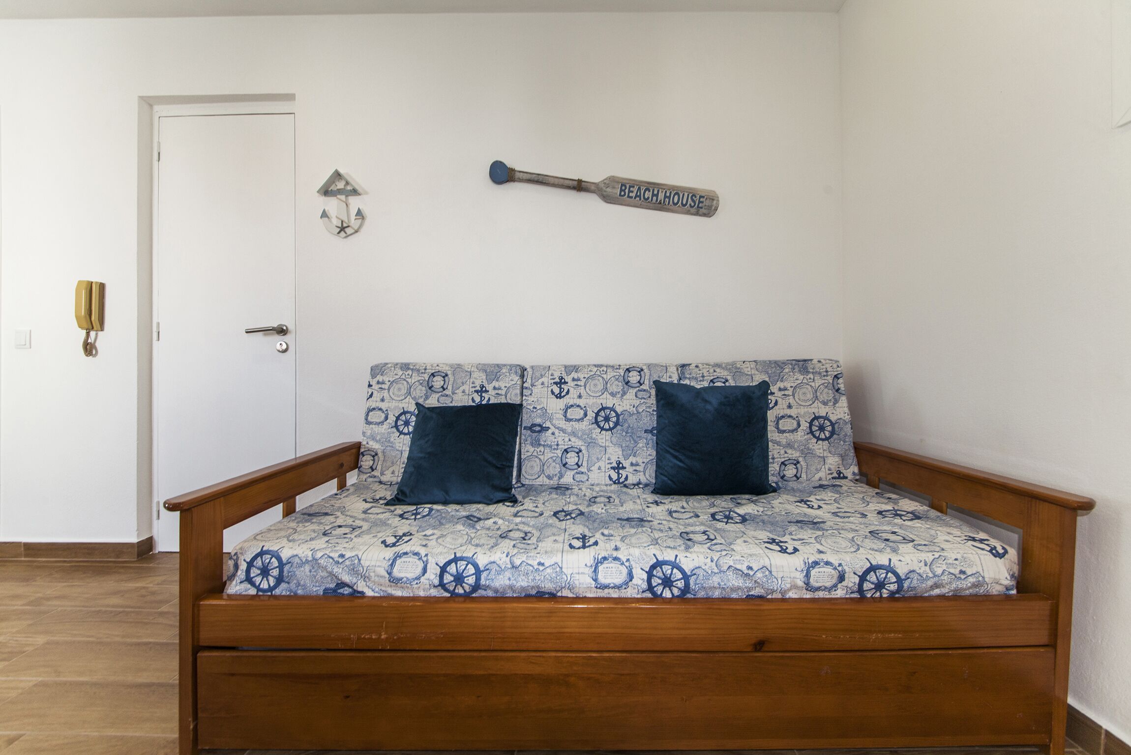 Una habitación pequeña con una cama de madera, dos almohadas, un reloj de pared y un bate de béisbol colgado en la pared.