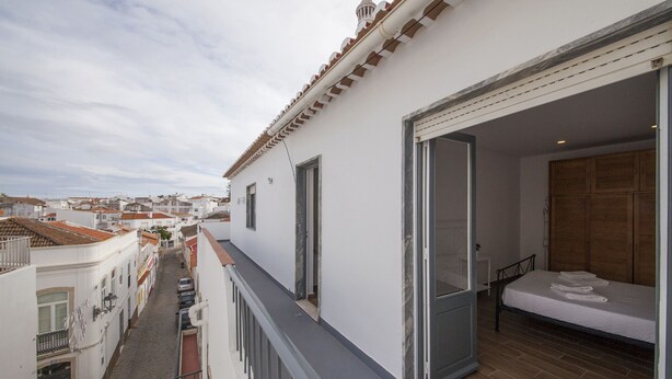 Un balcón con vistas a la calle, una cama con cabecera de madera y una puerta que da a otra habitación.