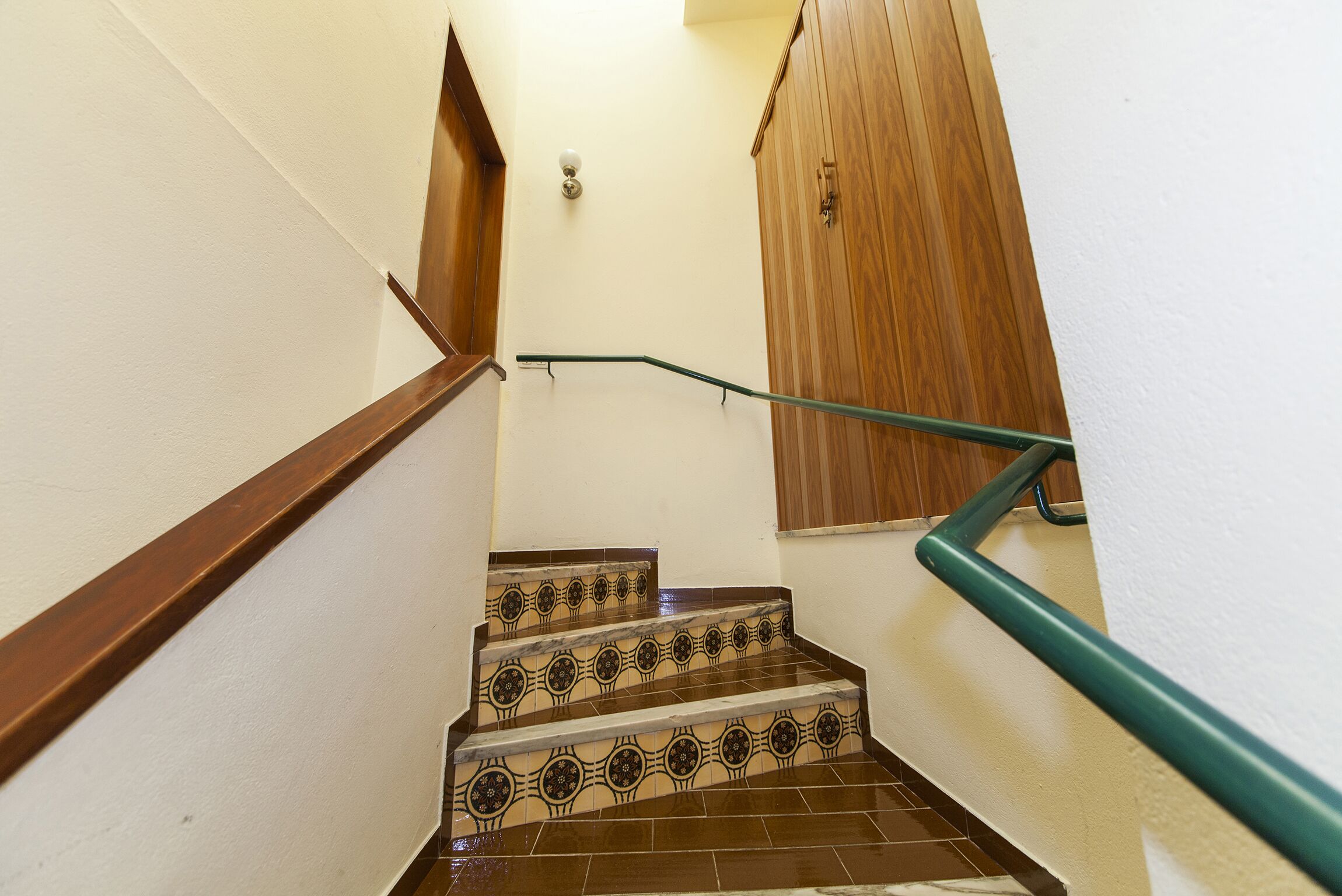 Una scala con piastrelle decorate e una ringhiera in legno.