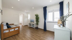 Una habitación amplia con una cama de madera, una planta en maceta, un armario blanco y una ventana con cortinas azules.