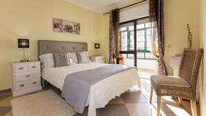 A bedroom with a bed, nightstands, a chair, a window with curtains, and a wall art piece. - B17 - The Stunning Seaview Apartment (Lagos)