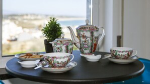 A table with a teapot, cups, and saucers, a small plant, and a bowl of cookies by a window overlooking a beach. - B17 - The Stunning Seaview Apartment (Lagos)