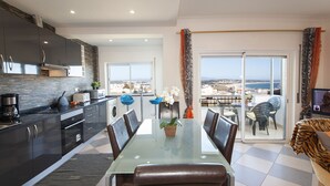 A modern kitchen with dark cabinets, a glass dining table, and a view of the city through large windows. - B17 - The Stunning Seaview Apartment (Lagos)