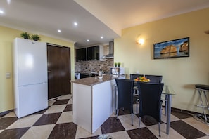 A modern kitchen with a central island, a refrigerator, and a dining area with chairs and a table. - B47 - Walkway Beachview Place (Lagos)