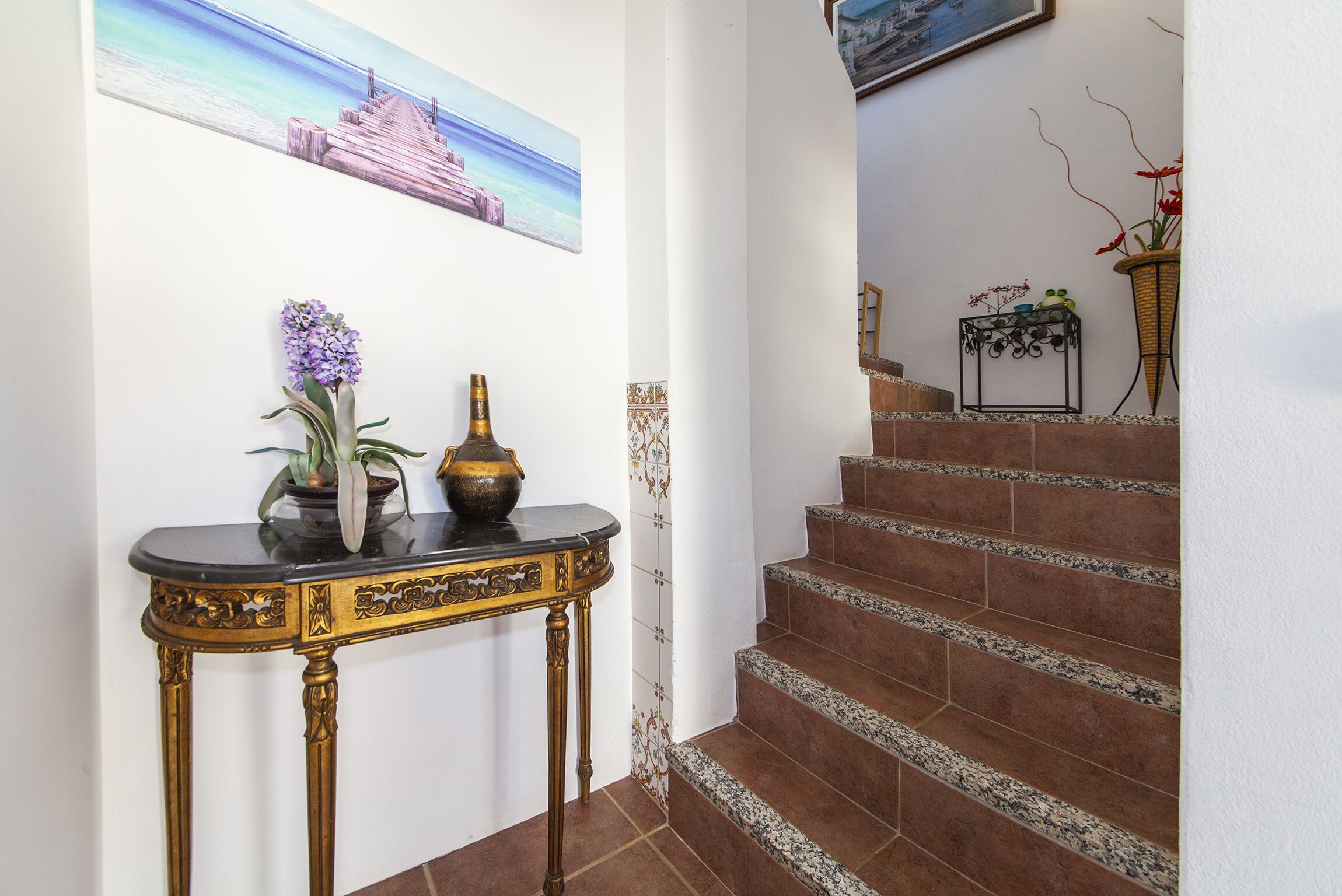 A staircase with brown tiles and a black console table with a vase of purple flowers.