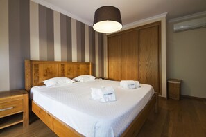 A neatly made bed with white linens and two towels, a wooden headboard, a bedside table with a drawer, a hanging lamp, a wardrobe, and a wicker basket. - C15 - The Patio do Convento Apartment (Lagos)