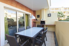 A balcony with a glass door, wicker furniture, a table, chairs, a hanging light, and a small shelf with items. - C15 - The Patio do Convento Apartment (Lagos)
