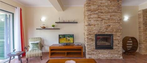 A living room with a stone fireplace, a television on a wooden stand, a striped armchair, and a small table with a bowl.