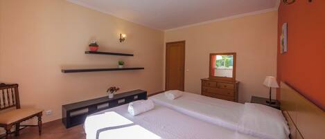 A bedroom with two beds, a wooden chair, a dresser, a mirror, and wall-mounted shelves with plants.