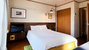 Une chambre à coucher bien rangée, avec un grand lit, une table de chevet sur laquelle se trouve un téléviseur, et un luminaire fixé au mur.