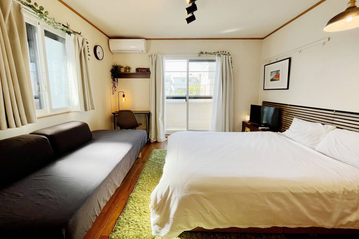 A hotel room with a bed, a sofa, a desk, a TV, and a window with curtains.