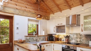 A wooden interior with a kitchen area featuring a wooden table, chairs, a stove, and cabinets. - Porthole Log Cabin (Minehead)