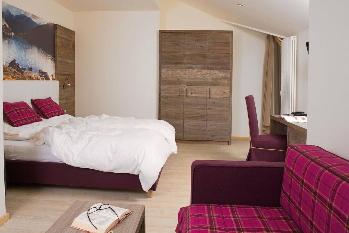 A bedroom with a bed, a desk, a chair, and a sofa.