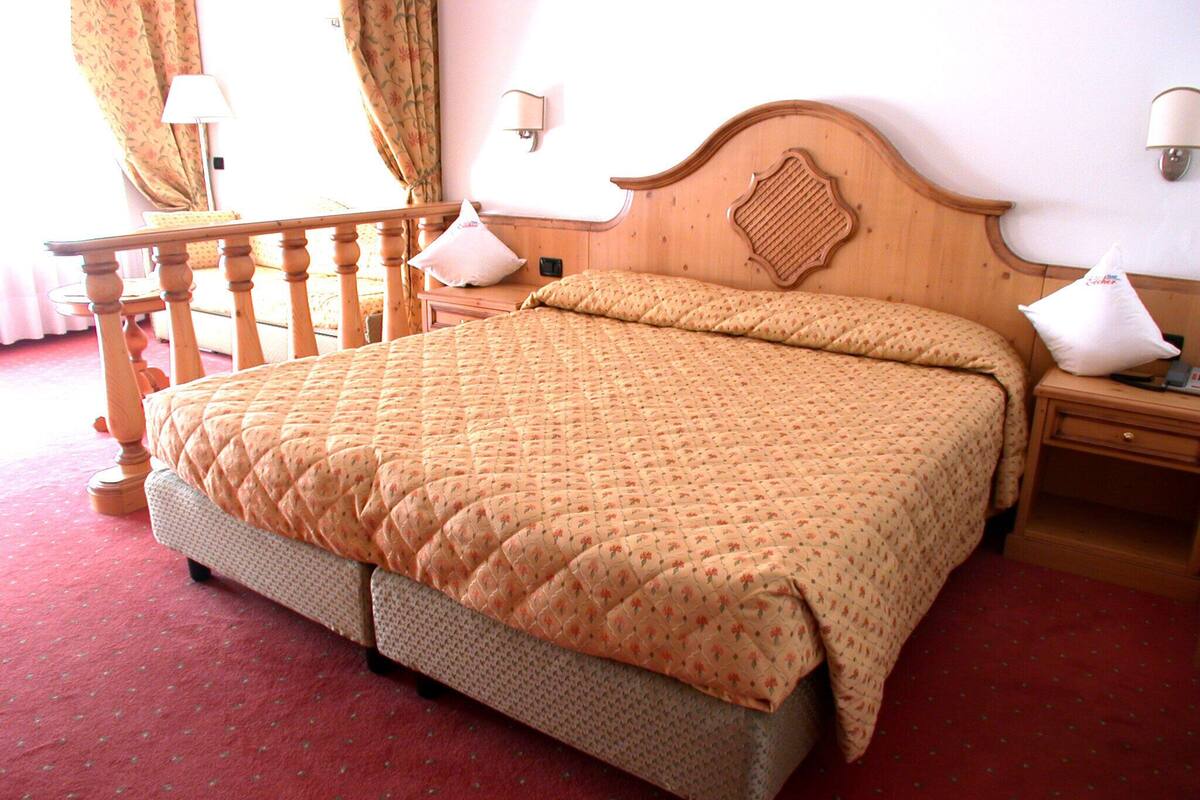 A neatly made bed with a quilted cover, a wooden headboard with a decorative pattern, and a wooden nightstand with a lamp.