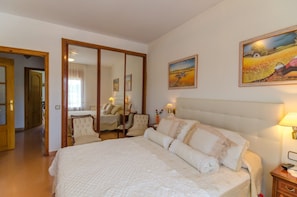 A bedroom with a large bed, a chair, a nightstand, and two paintings on the wall.