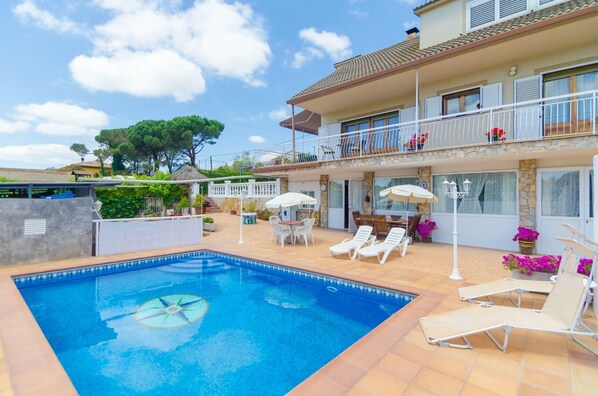 A swimming pool with lounge chairs and umbrellas, a covered patio, and a two-story building with balconies.