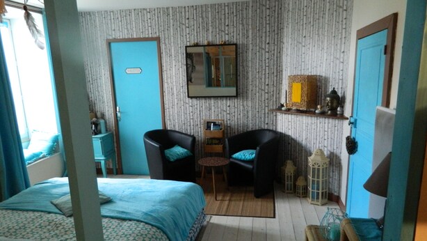 Una habitación con una cama, dos sillas, una mesita, un espejo y una puerta con la etiqueta 'TOILETRIES'.