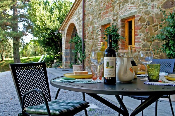An outdoor dining area with a stone building in the background, a bottle of wine, and various tableware.