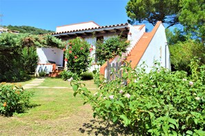 Uma casa com telhado de telhas vermelhas, fachada branca e escadaria de madeira que dá acesso à entrada.