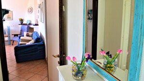 A room with a sofa, a small table with a vase of flowers, and a mirror with a blue frame. - New valmar Villa Camboni (Costa Rei)