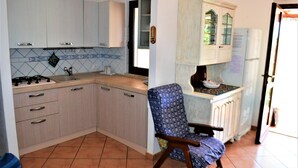 A kitchen with light-colored cabinets, a patterned chair, and a tiled backsplash. - New valmar Villa Camboni (Costa Rei)