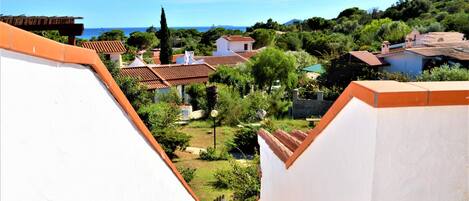A residential area with terracotta-roofed houses, a clear blue sky, and a view of the sea.