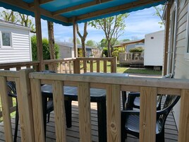 A wooden deck with a covered area, outdoor furniture, and a view of mobile homes in the background.