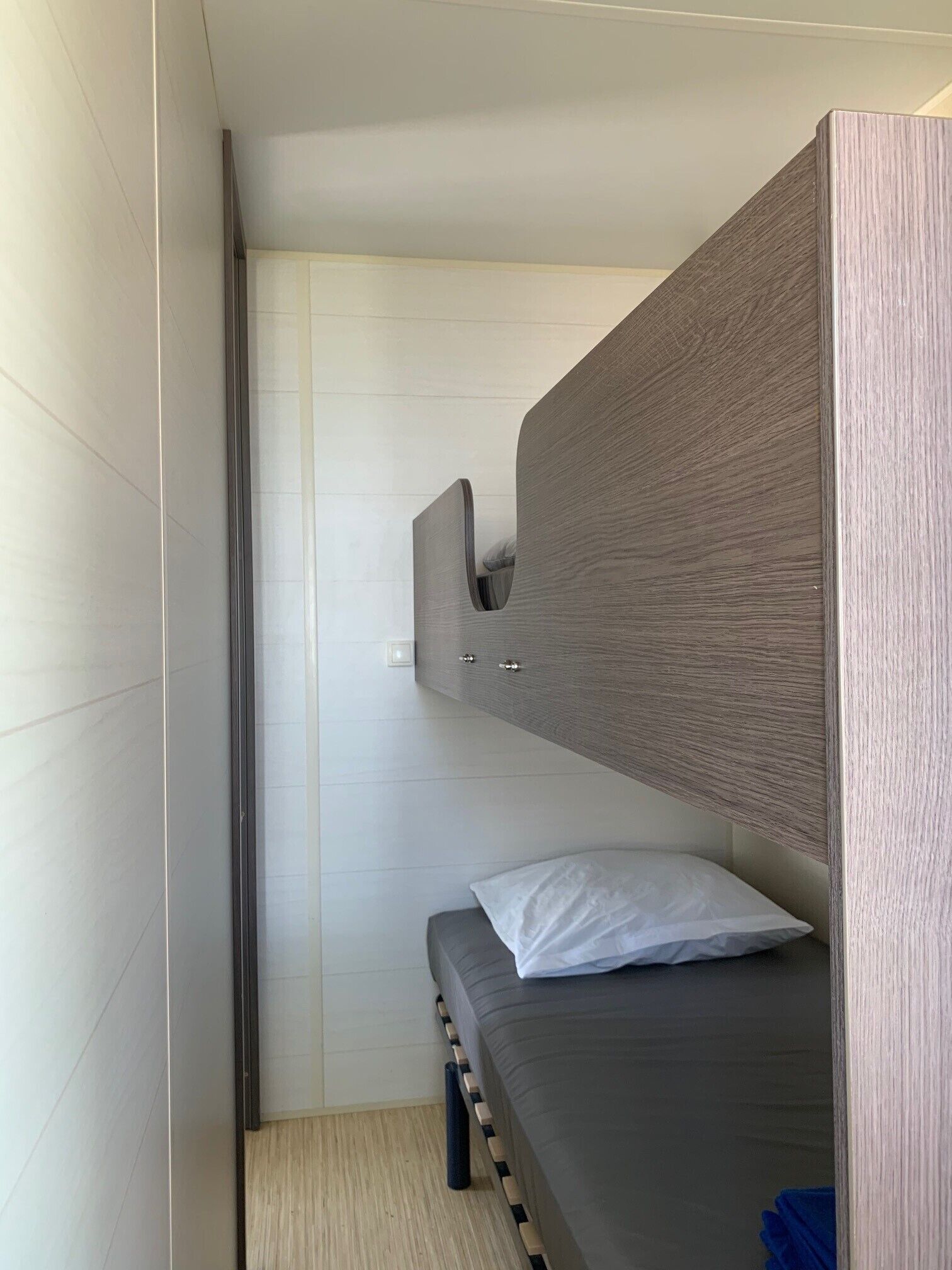 A compact, modern room with a bunk bed, a small bedside table, and a wall-mounted cabinet.