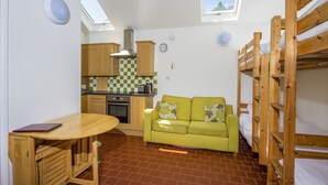 A compact room with a kitchenette, a sofa, a table, and bunk beds. - The Little Bunk House (Oswestry)