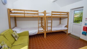 A dormitory room with bunk beds, a green sofa, a window with a view, and a fire safety panel. - The Little Bunk House (Oswestry)