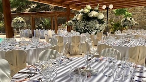 Un salón de banquetes con mesas redondas dispuestas para un evento formal, con manteles blancos, cubertería ordenada y centros de mesa florales.