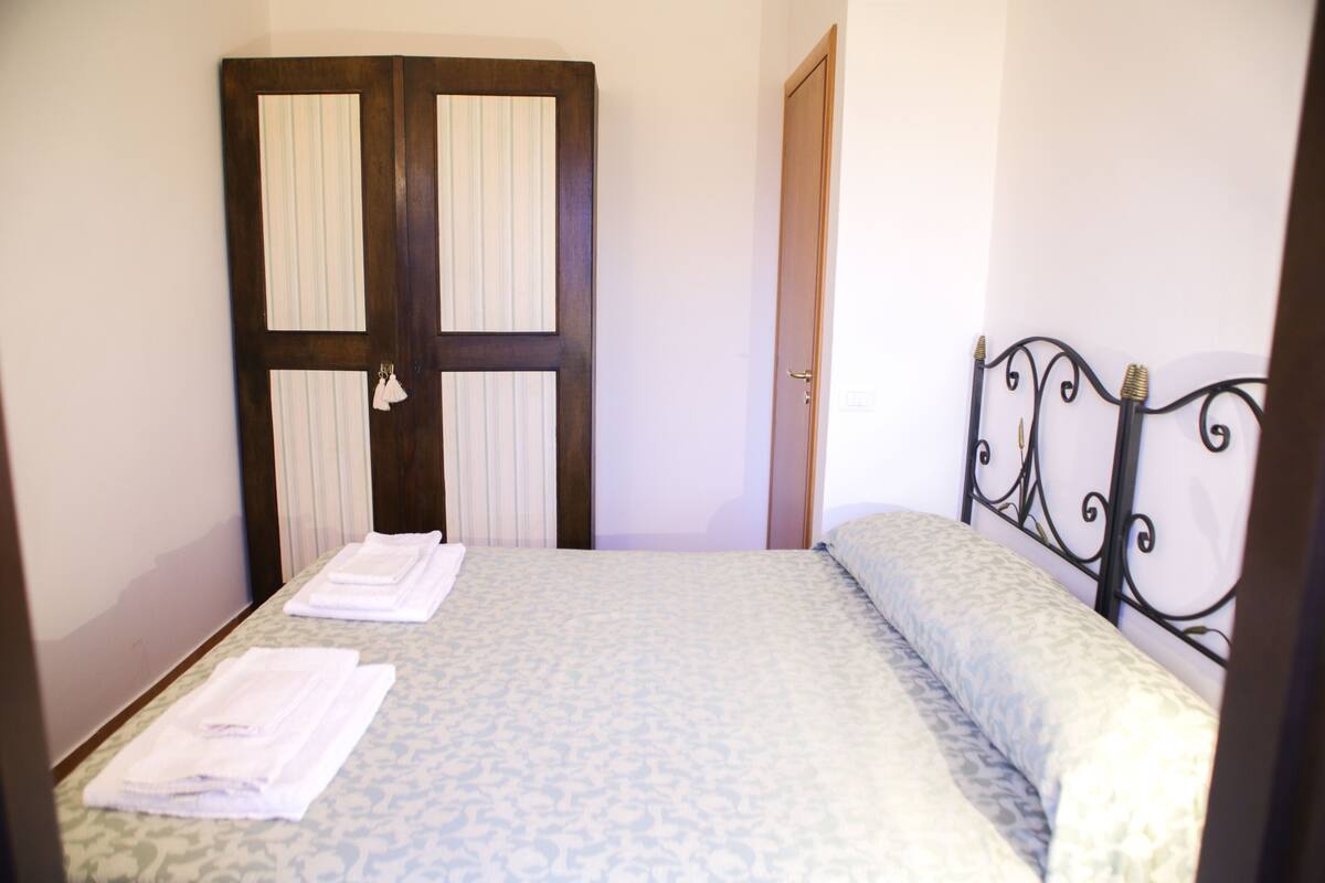 A hotel room with a bed, a wooden door with a mirror, and a metal headboard.