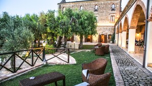 A courtyard with outdoor seating, a stone building, and a tree. - Masseria Mazzei Le Colline del Gelso (Corigliano-Rossano)