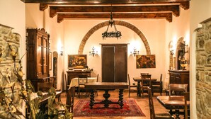 A dining area with a wooden table, chairs, and a red rug. There is a chandelier hanging from the ceiling, and a stone wall in the background. - Masseria Mazzei Le Colline del Gelso (Corigliano-Rossano)