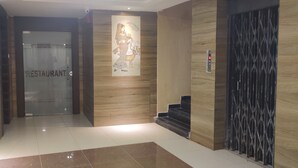 Un intérieur moderne avec une porte en verre portant l’inscription « RESTAURANT », un mur recouvert de panneaux en bois et un escalier menant à un étage supérieur.