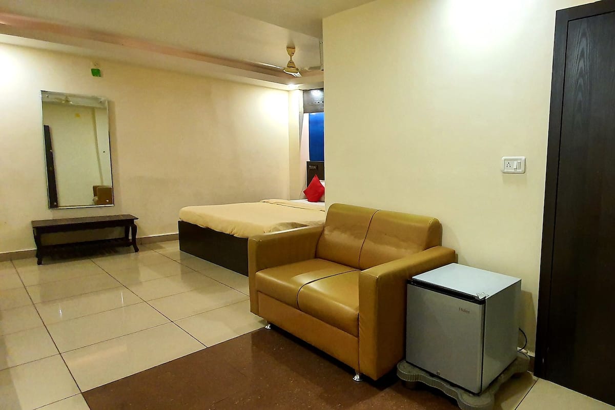 Ein Hotelzimmer mit Bett, einer kleinen Couch, einer Bank, einem Kleiderschrank und einem kleinen Kühlschrank.