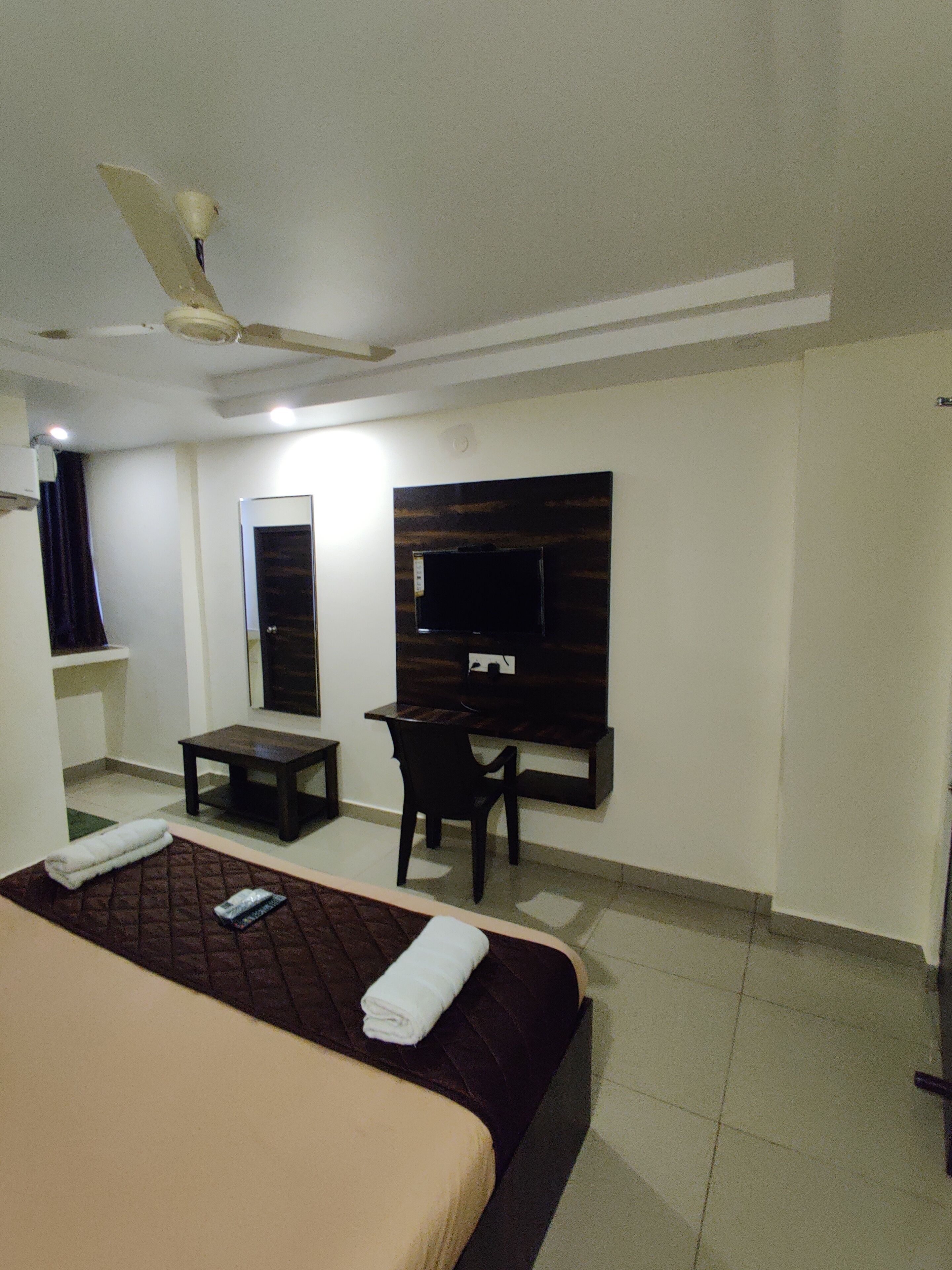 A hotel room with a bed, a desk, a chair, a TV, and a ceiling fan.