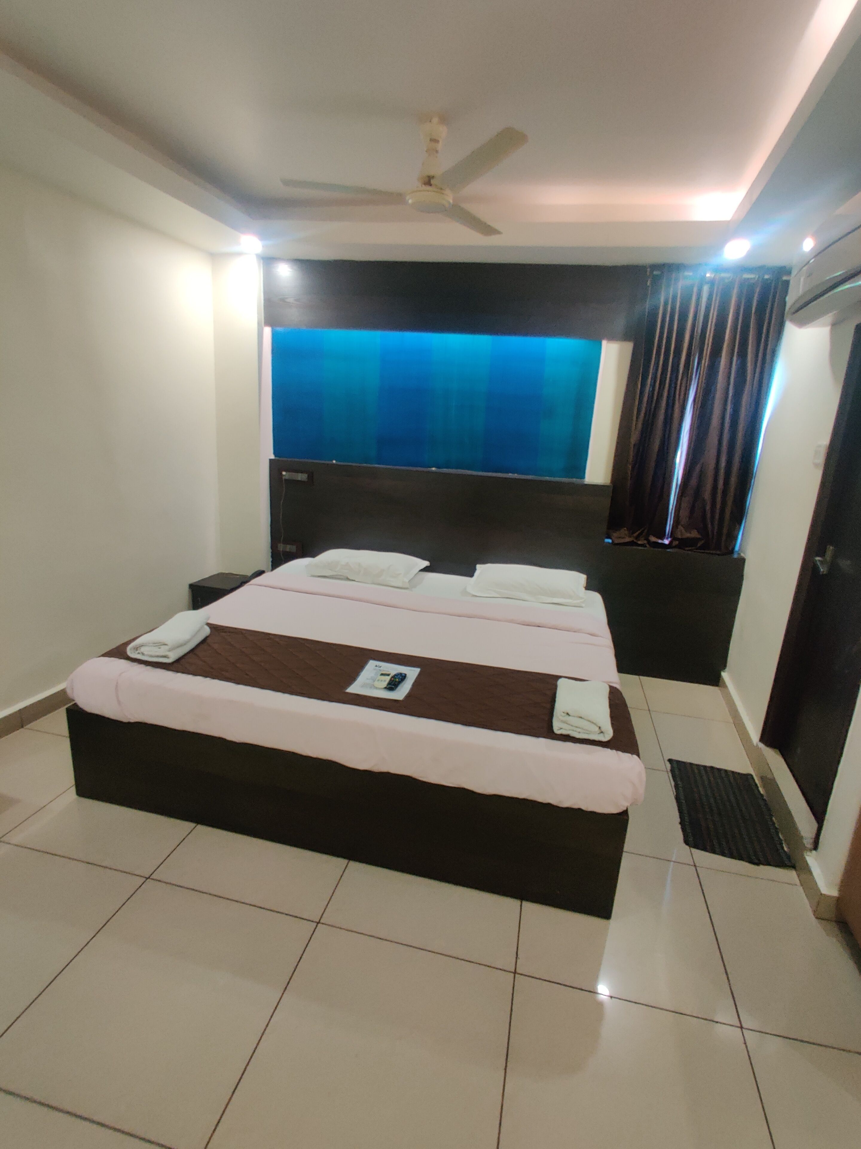 A bedroom with a bed, a ceiling fan, a nightstand, a window with curtains, and a door.