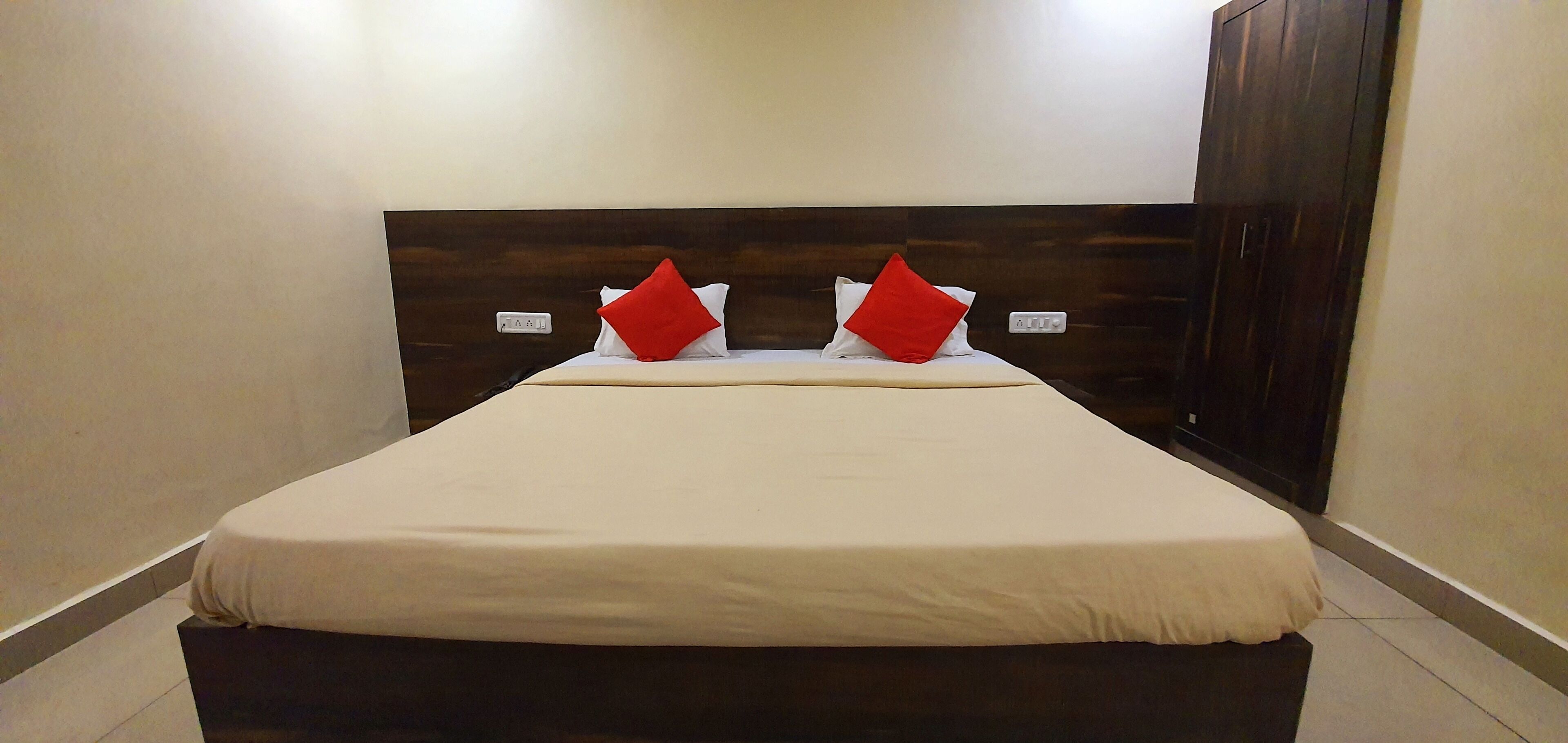 A hotel room with a large bed, dark wooden headboard, and two red pillows.